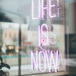 Urban scene with a glowing 'Life is Now' neon sign reflecting in a window, conveying a modern, motivational vibe.